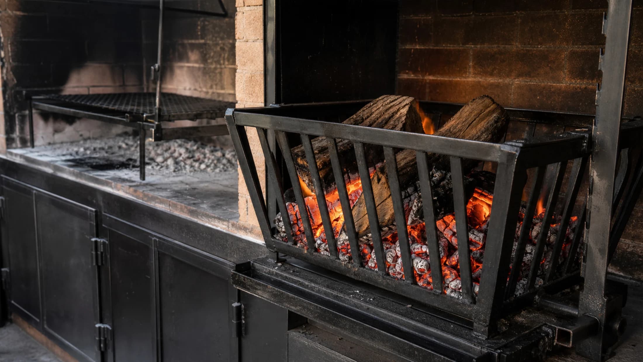 Fogonero brasero de hierro con leña y brasas junto a una parrilla argentina