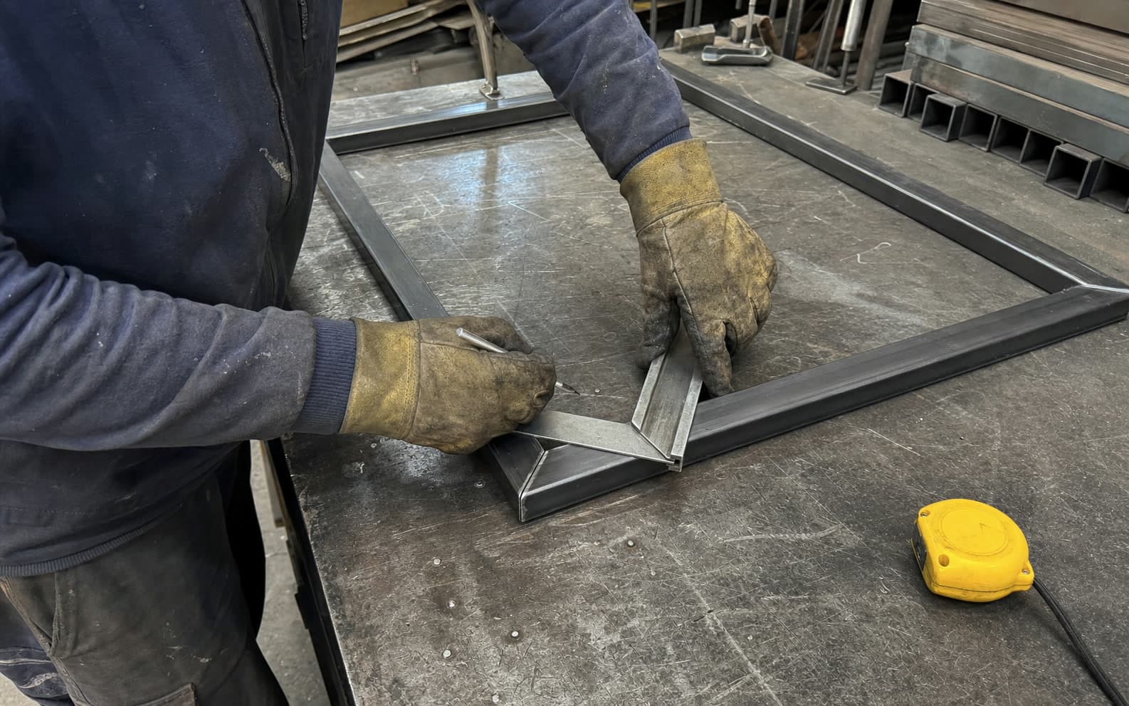 El herrero escuadrando y marcando perfiles de hierro a mano en la mesa del taller